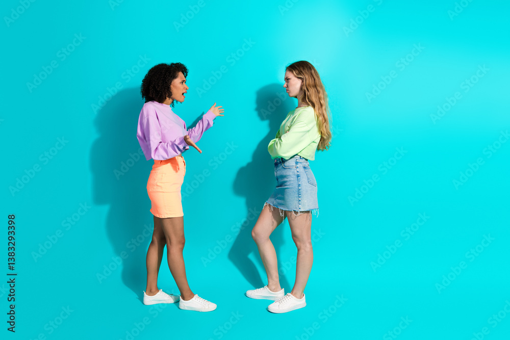 Obraz premium Two young women discussing against a vibrant turquoise background, showcasing modern summer fashion and casual style with stylish outfits.