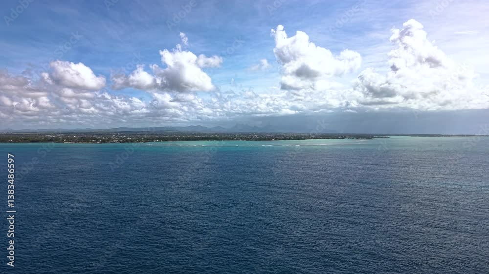 Dramatic Cloudscape Over Mauritian Coastline With Turquoise Shallows And Deep Blue Waters Against Mountain Backdrop Dramatic Cloudscape Over Mauritian Coastline With Turquoise Shallows And Deep Blue Waters Against Mountain Backdrop