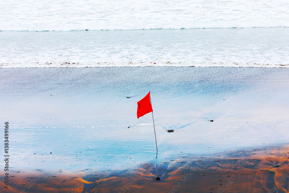 Beach conditions today require caution, as indicated by the red flag. Beach with red flag is prominently planted in the sand, serving as a clear warning or caution for visitors