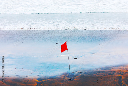 Obraz na płótnie Beach conditions today require caution, as indicated by the red flag. Beach with red flag is prominently planted in the sand, serving as a clear warning or caution for visitors w salonie