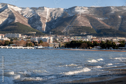 A beautiful mountain range with a city in the background. The city is full of buildings and the water is calm