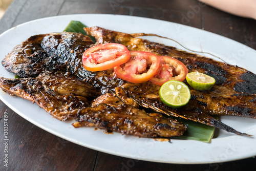 Grilled fish (ikan bakar) served with two chili sauces (sambal) on a green plate. Indonesian seafood dish