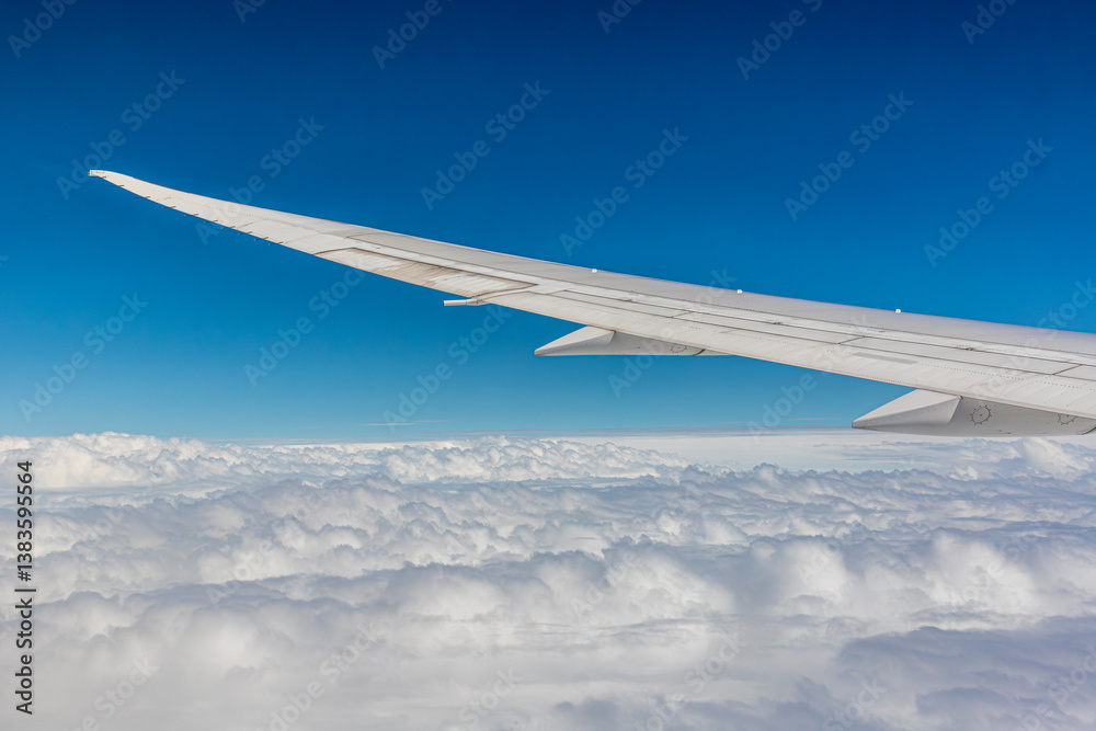 Left (port) wing of a Boeing 787-9 set against a blue sky over white clouds seen from the passenger window somewhere near Hong Kong