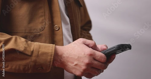 Man in brown shirt holding smartphone in his hand and typing on it. Concept of work anywhere, online communication technology and mobile worker.