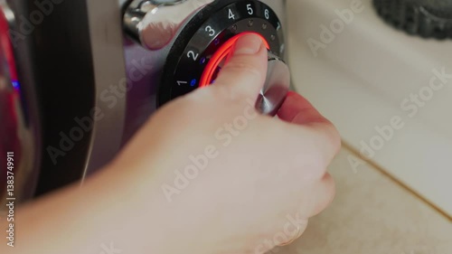 Close up of hand adjusting silver control knob of electric stand mixer with red and blue light indicators in cozy kitchen, showcasing operation of appliance in cooking or baking environment photo