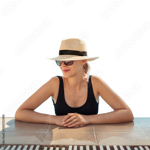 Girl in hat is in pool, leaning on side. Young woman with glasses and hat on vacation is relaxing on edge of pool on sunny day. Portrait of woman in pool looking at camera. Sitting on edge of pool