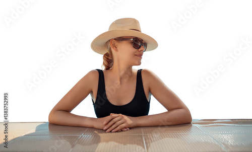 Girl in hat is in pool, leaning on side. Young woman with glasses and hat on vacation is relaxing on edge of pool on sunny day. Portrait of woman in pool looking at camera. Sitting on edge of pool