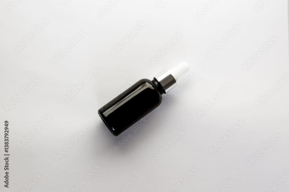 Black dropper bottle with pipette or glass container without label. Cosmetic product or serum or oil lies on white background, top view. Black dropper bottle with pipette or glass container without label. Cosmetic product or serum or oil lies on white background, top view.