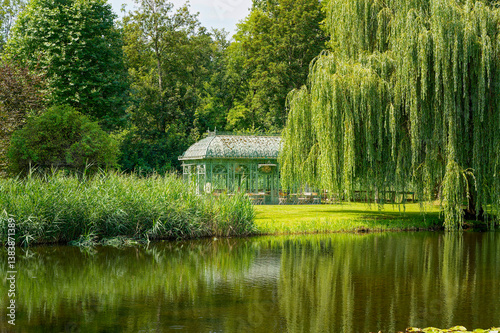View over a small pond, in which the trees are reflected, to a small pavilion.