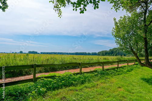 View to a path leading past a fence and between meadows.