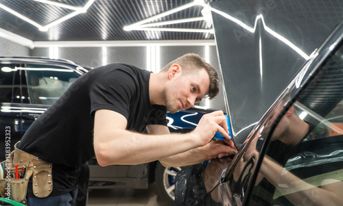The process of installing PPF, armored film on the car. PPF is a polyurethane, protective film that protects the paint from scratches. Car wrapping, tuning, styling. Close-up, selective focus.