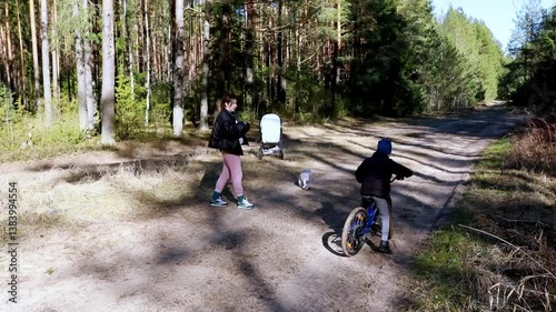 Family enjoys a day outdoors as child rides bicycle on forest path in springtime sunlight
