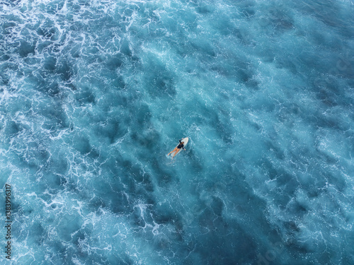 Aerial 90 degree straight down drone photo of a young female surfer on a surfboard in the emerald ocean water. Pacific Coast, El Tunco, El Salvador, Central America.