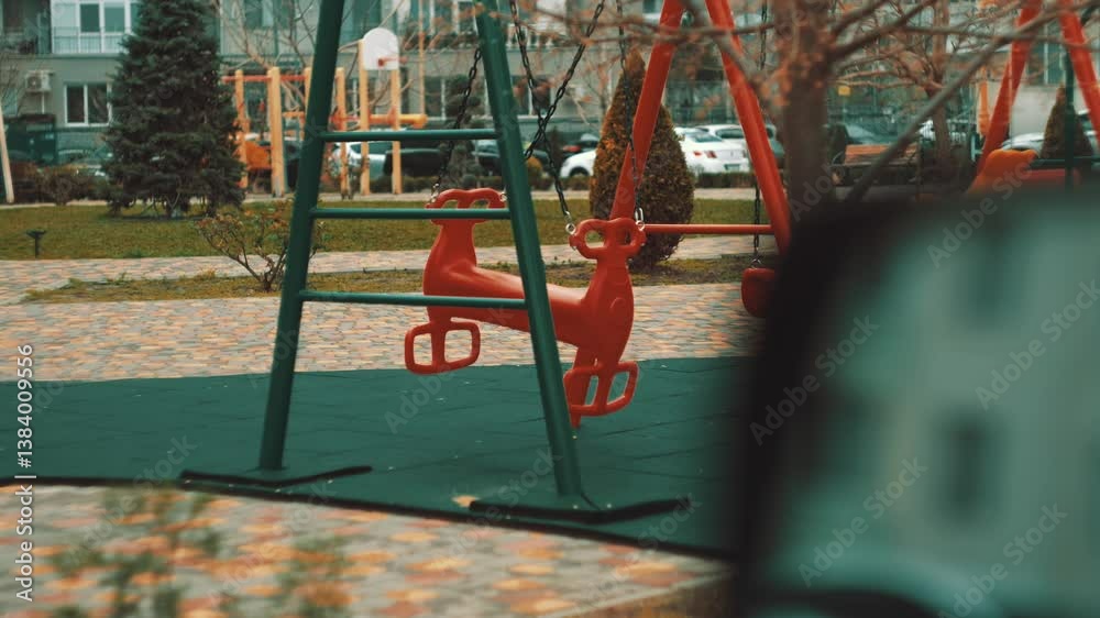 Windy day in a city courtyard. Colorful swings move slowly with the breeze in a quiet, modern housing complex Windy day in a city courtyard. Colorful swings move slowly with the breeze in a quiet, modern housing complex