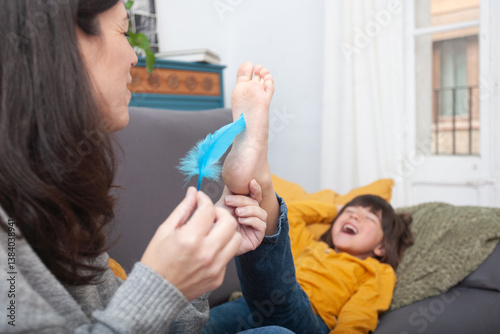 Mother tickling child’s bare feet with blue feather