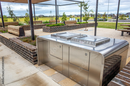 Fototapeta Naklejka Na Ścianę i Meble -  A modern outdoor community space in a new Australian housing development, featuring a stainless steel BBQ and cooking station, covered pavilion, and bench seating.A community public recreational space