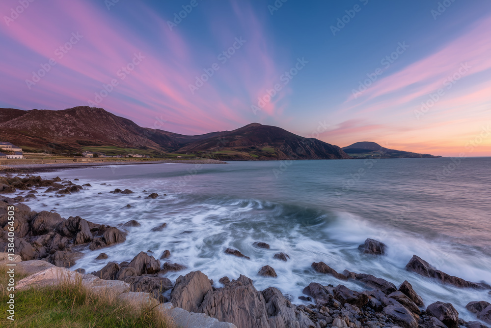 Fototapeta premium Rocky irish coastline at sunset with waves crashing onto shore, colorful pink clouds in blue sky and rolling hills in background
