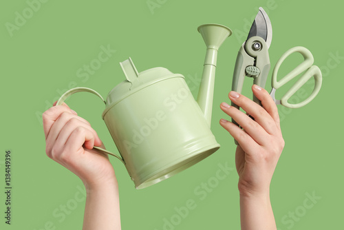 Obraz na płótnie Female hands with watering can, pruner and scissors on green background w salonie