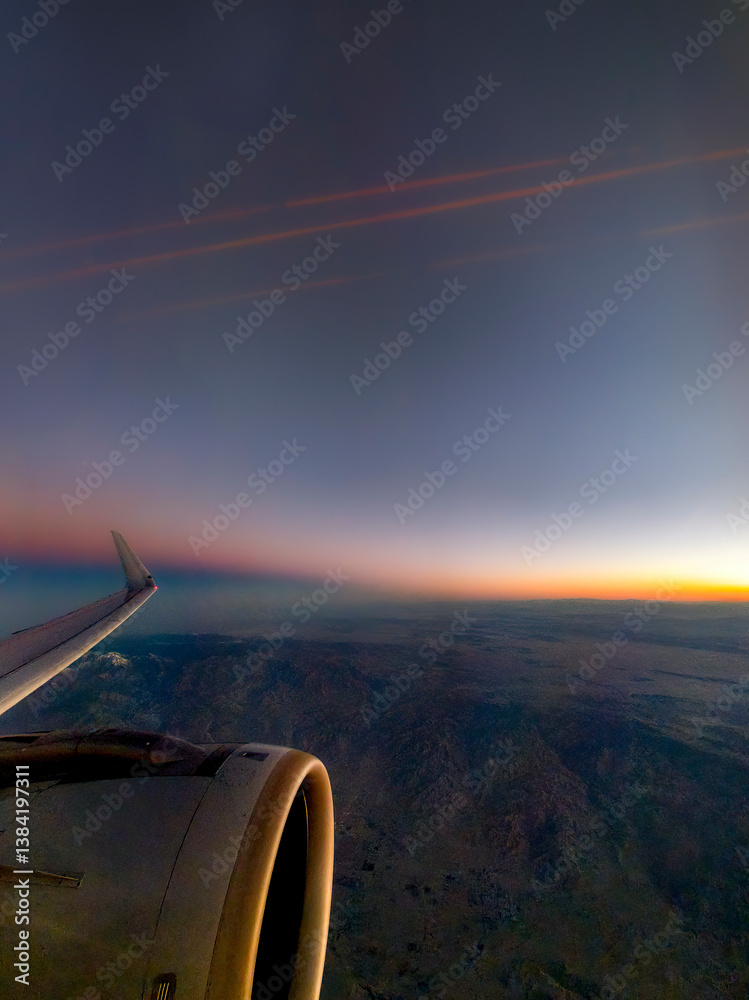 Looking out the window of an airplane with partial wing and engine view with dramatic landscape and sky