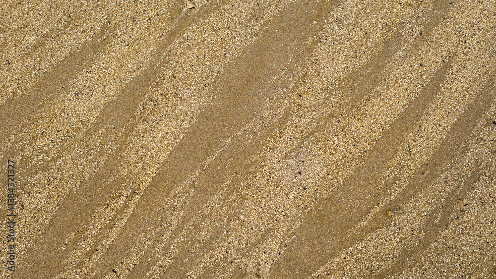 Diagonal close-up of textured beach sand with fine grains and natural wavy patterns. The intricate surface highlights the effects of wind and water erosion, creating a mesmerizing abstract design. Diagonal close-up of textured beach sand with fine grains and natural wavy patterns. The intricate surface highlights the effects of wind and water erosion, creating a mesmerizing abstract design.
