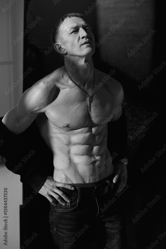 Naklejka premium Slim muscular male model on black background. Shirtless fitness guy in black sweatpants posing in studio. Man with six pack abs in sunset light. Brutal photo