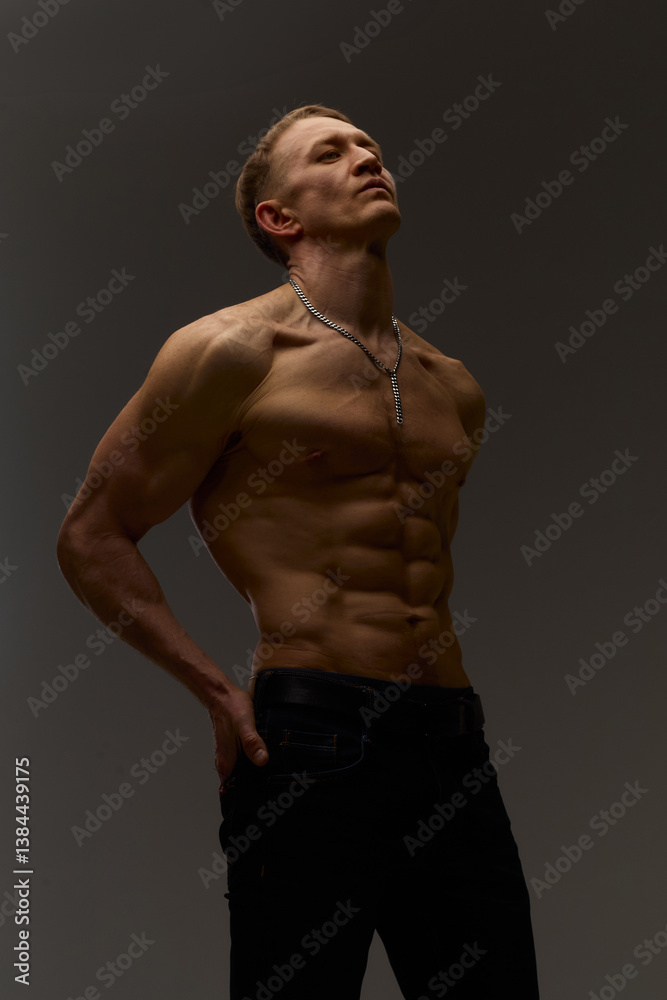 Fototapeta premium Slim muscular male model on black background. Shirtless fitness guy in black sweatpants posing in studio. Man with six pack abs in sunset light. Brutal photo