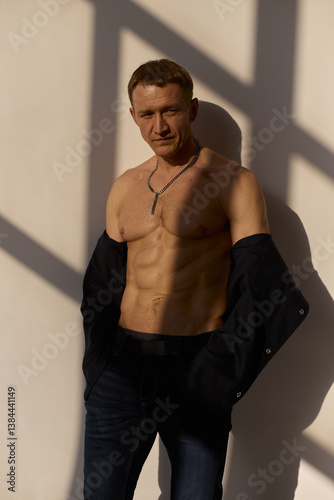 Slim muscular male model on black background. Shirtless fitness guy in black sweatpants posing in studio. Man with six pack abs in sunset light. Brutal photo