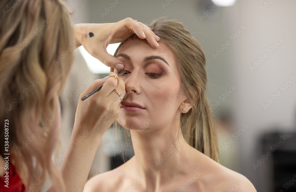 Fototapeta premium Woman is getting her makeup done by makeup artist. The woman doing the makeup is using a brush to apply it