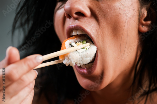 Sushi in woman mouth. Sexy woman eating sushi with chopsticks. Model eat sashimi. Sensual bite of sushi. Female tasting nigiri. Lunch at Japanese restaurant. Desire for delicious sushi. Asian food.
