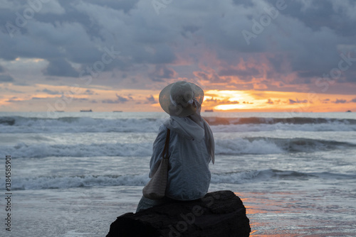 A woman sits alone and enjoys the view of the beach at sunset