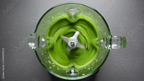 Green smoothie being made in a glass blender sitting on a gray table