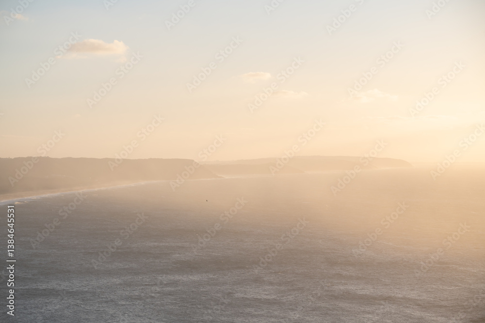 Atlantic ocean coast in Nazare, Portugal. Pink clouds over the ocean at foggy sunset.
