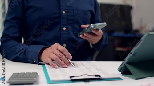 Analyzing Financial Data Person In Blue Shirt Reviews Document With Pen, Calculator, Clipboard, Tablet Screen Boosting Productivity Reviewing Statistics On Medium