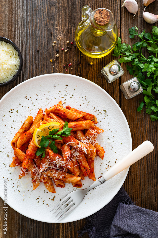 Penne noodles with tomato sauce and parmesan cheese served on wooden table