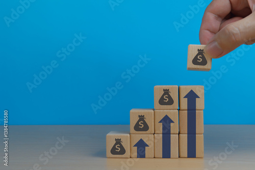 More profit, human hand placing more money bag icons on the growth graph