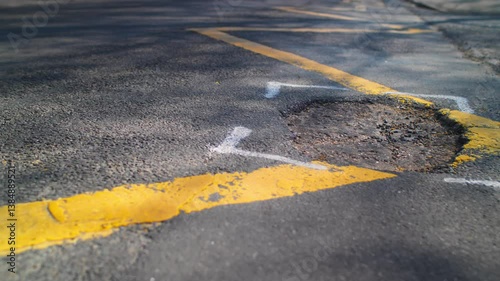 A large area of pothole tarmac damage in a suburban British street. The hole is highlighted for repair. 