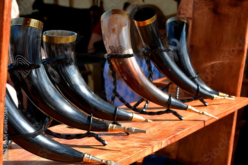 A close up on a set of massive horns and cups decorated with golden elements and having some carvings on them, displayed during a viking and medieval themed festival organized in Poland in summer