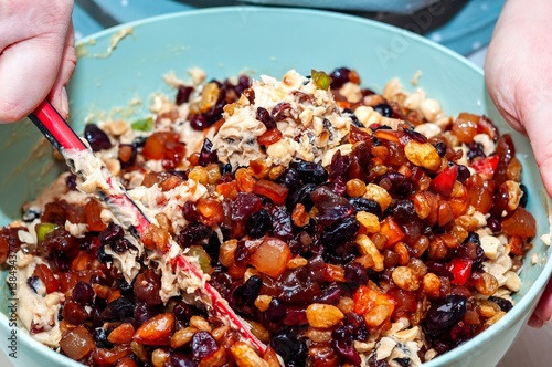 Valokuva Hands mixing a colorful medley of fruit and nuts to make a delicious fruitcake from scratch