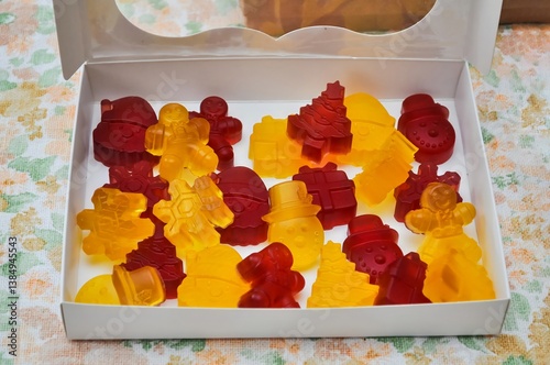 Colorful, festive gummy candies in various Christmas shapes, presented in a white box.