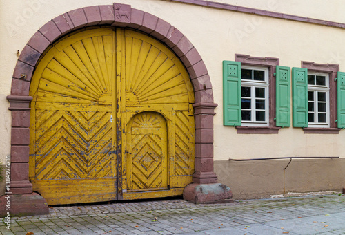 Old, weathered wooden courtyard gate with sandstone surround and windows with wooden shutters on an old building in Germany