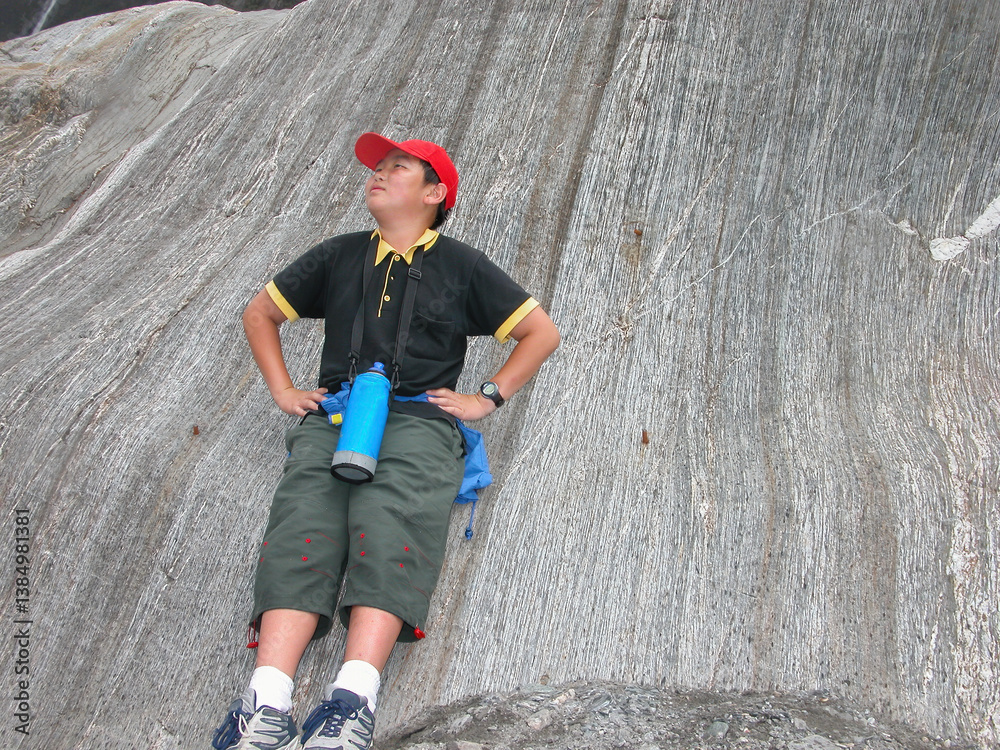 Teenage boy leaning on glacier rock and posing for fun photos. Franz Josef Glacier. South Island. New Zealand.
