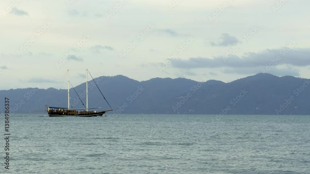 A wide shot depicts a sailing ship powered by its engine, moving smoothly across the still, slightly rippled sea with its sails down. The vessel leaves a faint trail in the water under a soft, cloudy A wide shot depicts a sailing ship powered by its engine, moving smoothly across the still, slightly rippled sea with its sails down. The vessel leaves a faint trail in the water under a soft, cloudy