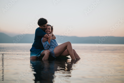A couple share a joyful and intimate moment in a serene lakeside setting at sunset, expressing love and happiness. The tranquil environment enhances the mood of connection and romance.