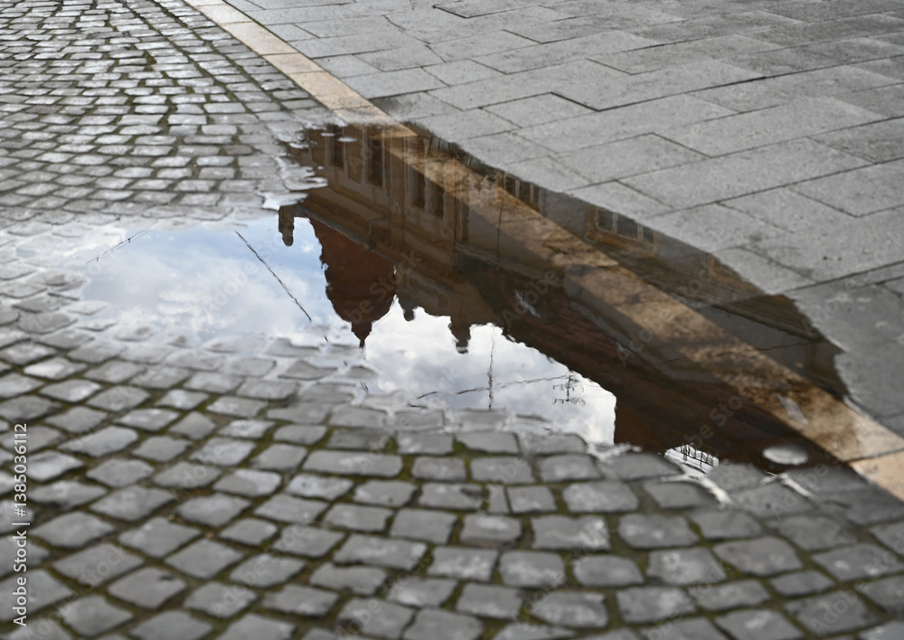 Reflections of historic architecture in a puddle on cobblestone street