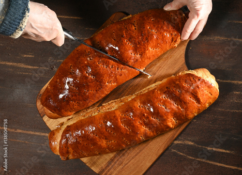 Obraz na płótnie Freshly baked bread being sliced on a wooden board in a cozy kitchen setting during the afternoon w salonie