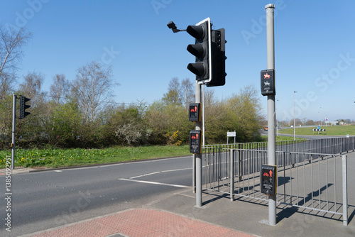 Multi level, standard, high and low, push button traffic lights for pedestrians, cyclists and horse riders next to a road with a blue sky in the distance.
