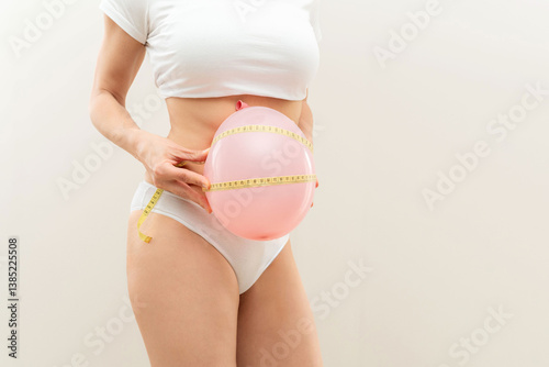Foto Close up of Woman holding inflated pink balloon and measuring tape on belly, die