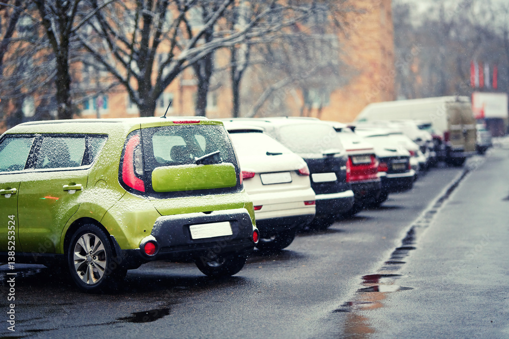 Parked cars covered with fresh snow in residential urban street, showing seasonal weather, outdoor transportation, quiet frosty atmosphere. Frozen cars lined up on road, cold weather. Selective focus