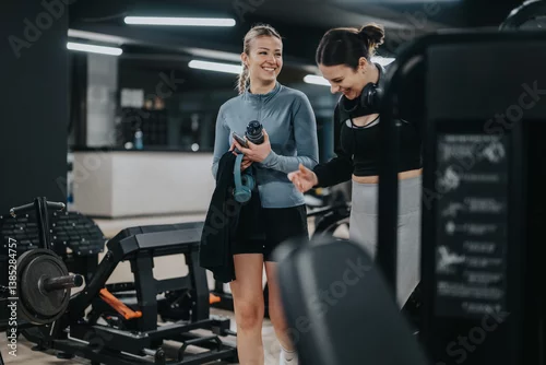 Panel kuchenny z motywem Two women in fitness attire share a laugh and chat while working out in a modern gym setting surrounded by gym equipment.