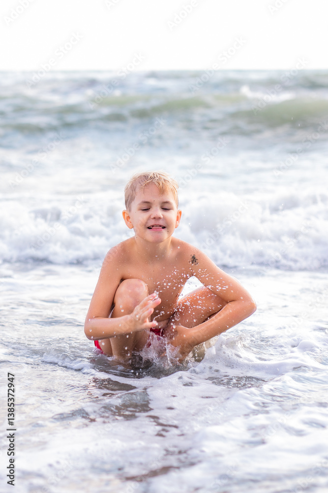 Boy playing with waves while squatting on sandy beach at sunset Boy playing with waves while squatting on sandy beach at sunset